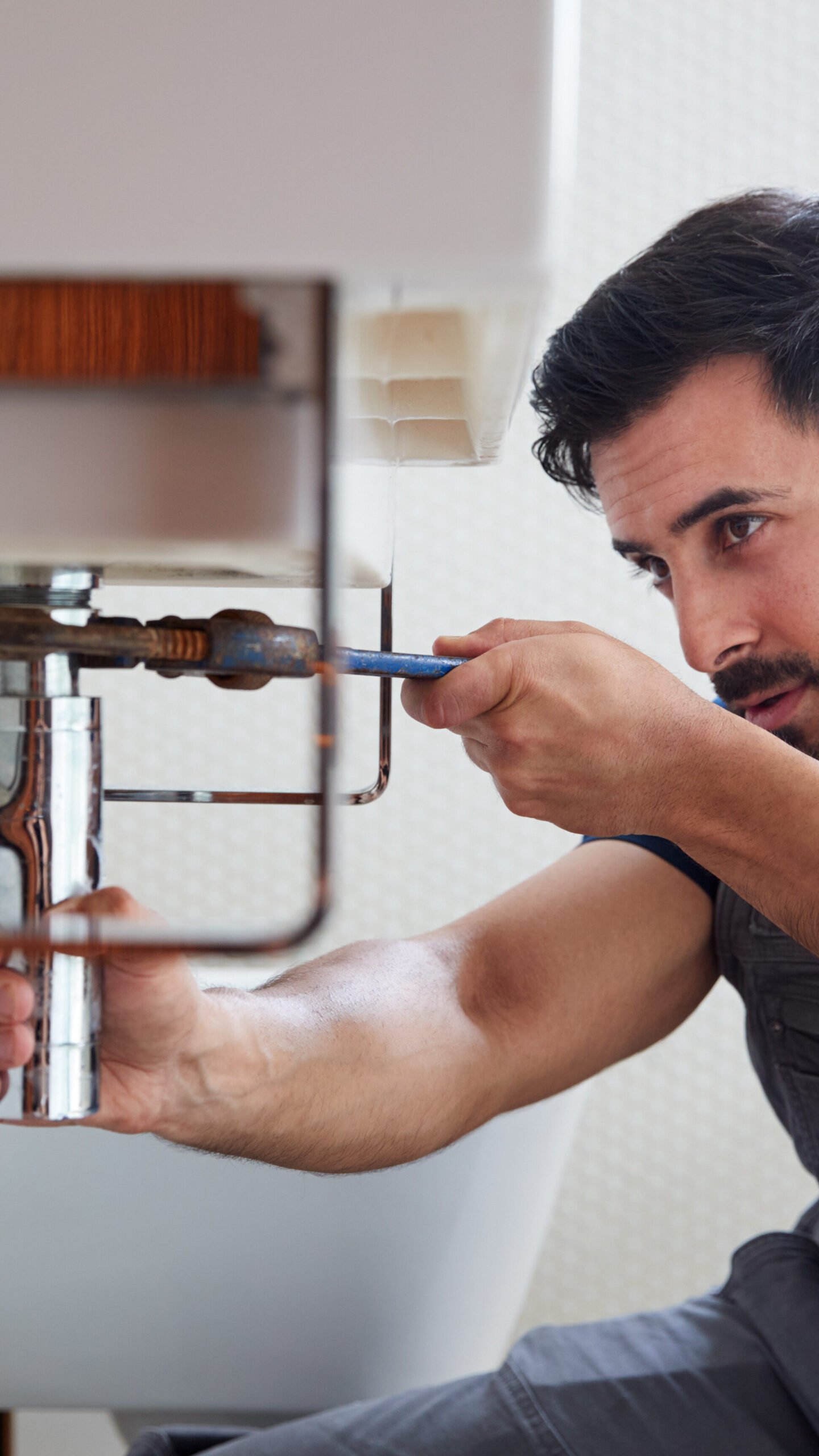 male plumber using wrench to fix leaking sink in home bathroom